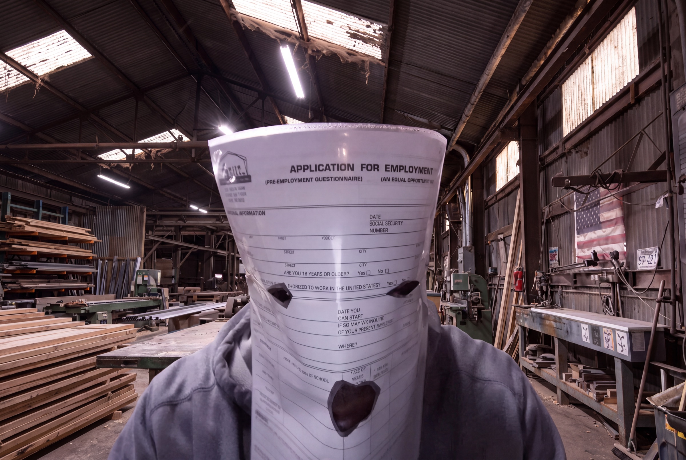 A man wearing a blank job application as a mask, standing in a workshop